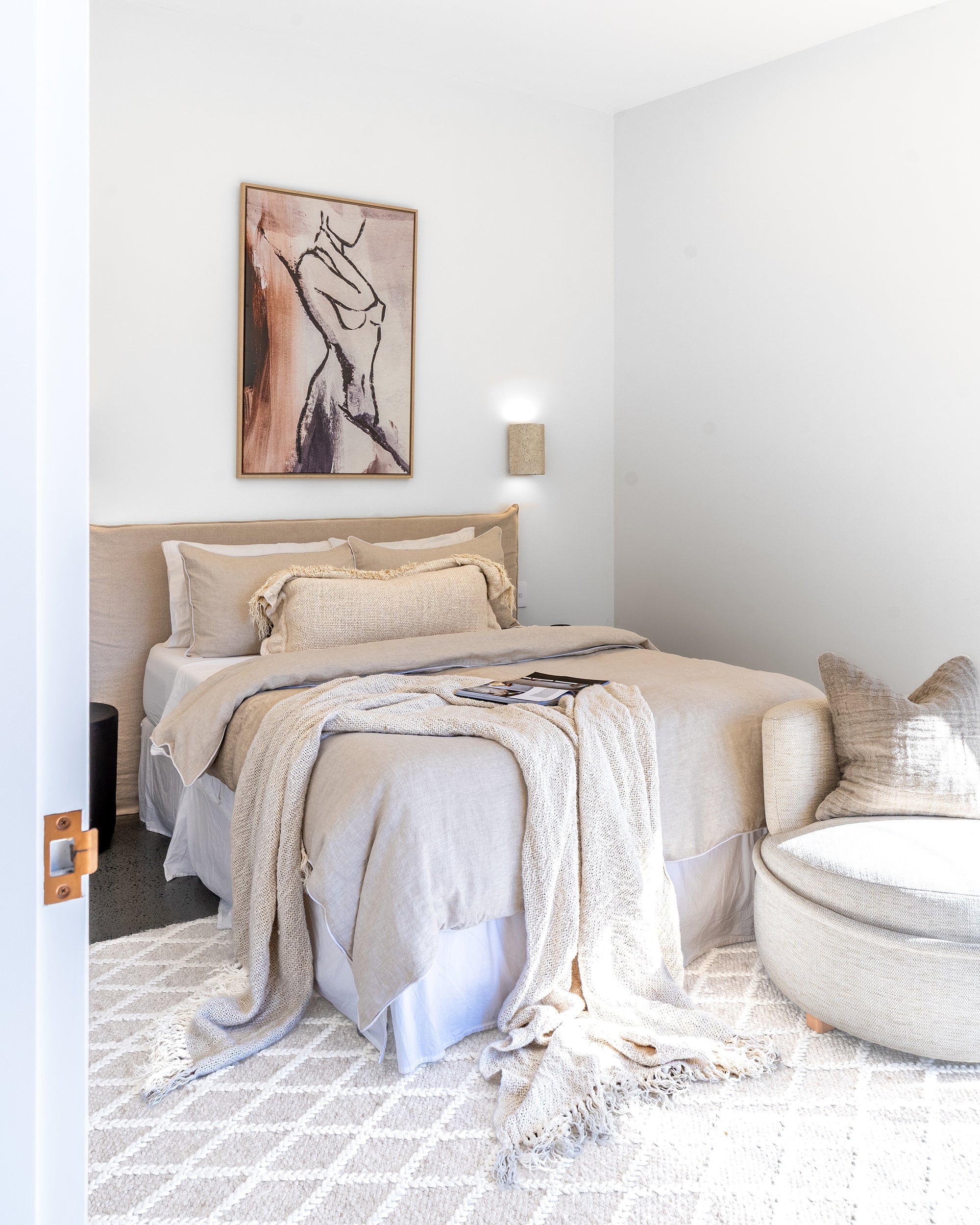 Tranquil bedroom featuring a bedhead in natural linen, styled with layered bedding and a round occasional chair in a soft, light-filled setting
