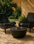 Pair of black congo rattan loungers styled in a sunny outdoor garden setting with a round black kisiki coffee table and two drinks