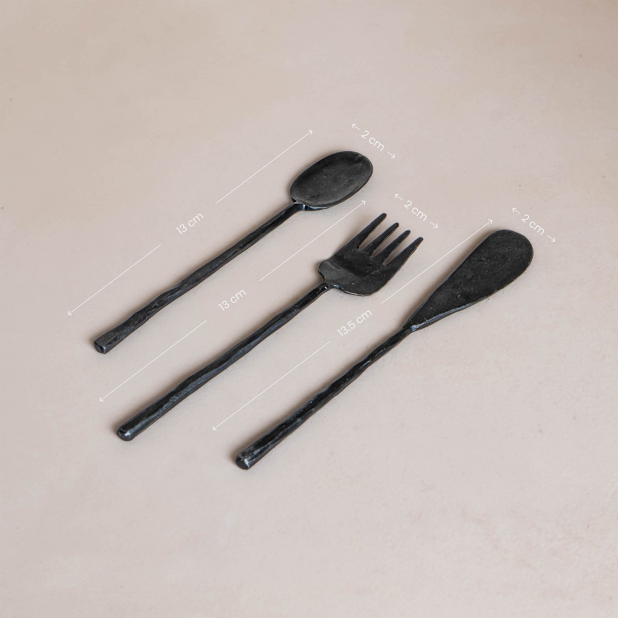 A set of three handcrafted black cutlery pieces from KULALA Living, including a spoon, fork, and knife, featuring a hand-forged finish with textured handles for a refined yet rustic dining aesthetic