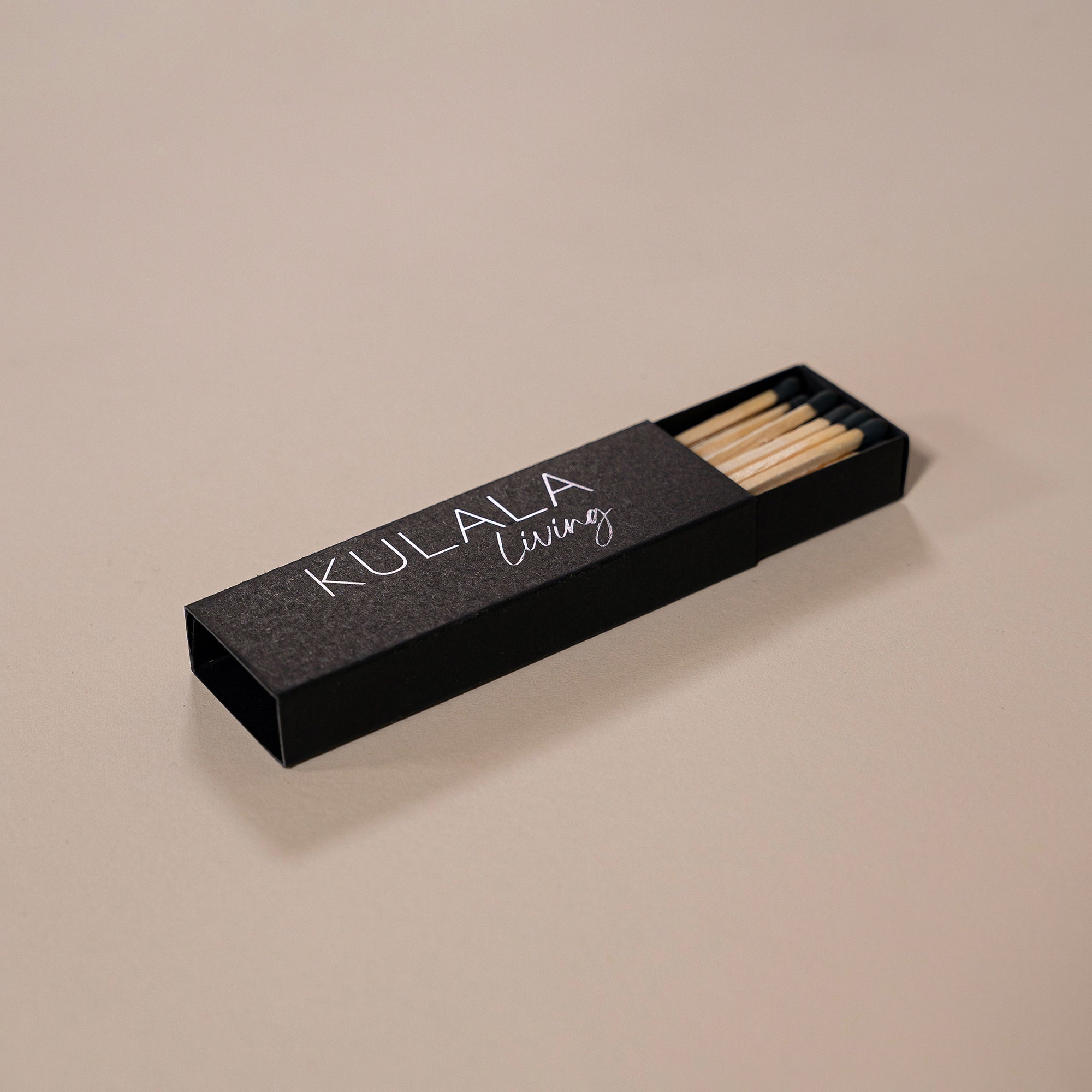 Kulala Living black matchbox with minimalist branding, featuring long wooden matches with black tips, set against a neutral backdrop for a refined aesthetic