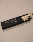 Kulala Living black matchbox with minimalist branding, featuring long wooden matches with black tips, set against a neutral backdrop for a refined aesthetic