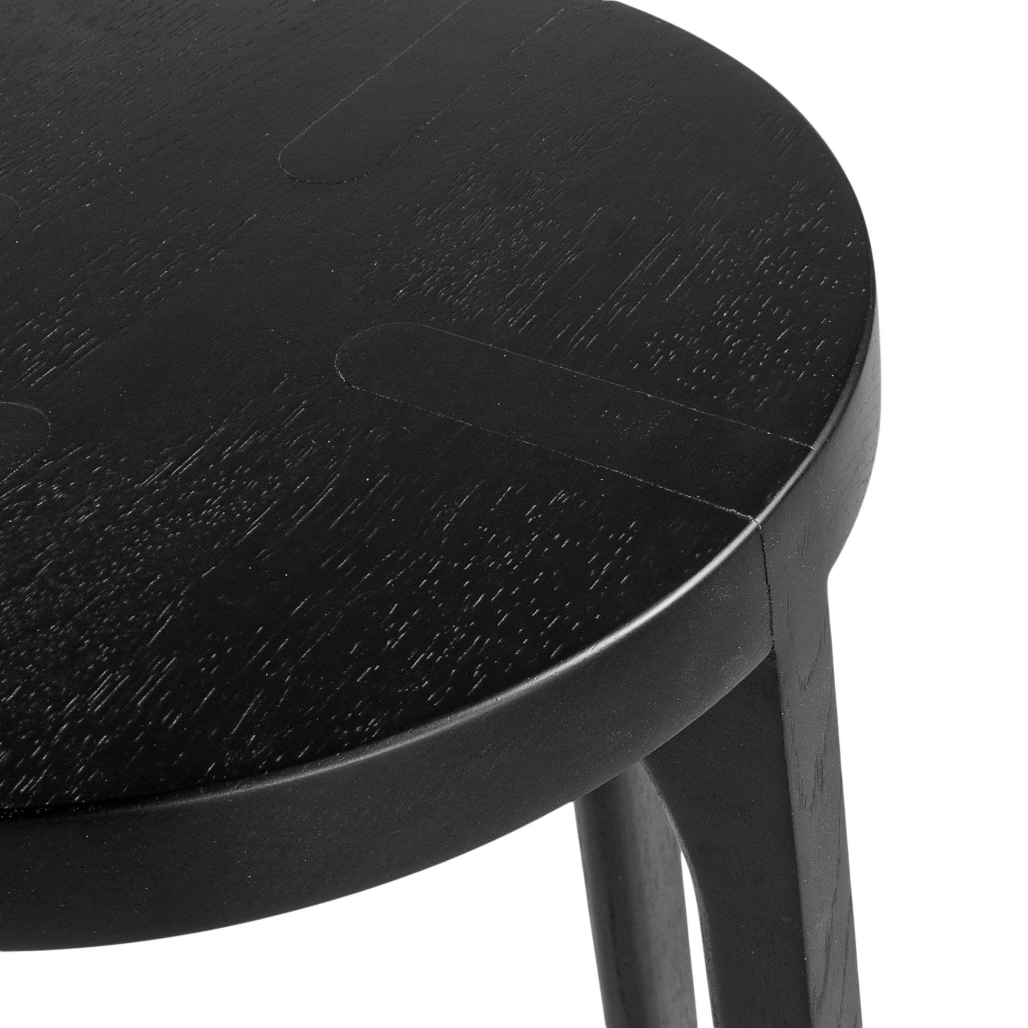 A sleek black oak round stool featuring a minimalist design with subtly curved legs. Crafted from solid oak with a matte black finish, this versatile piece functions as a stool or side table, adding a modern touch to any space