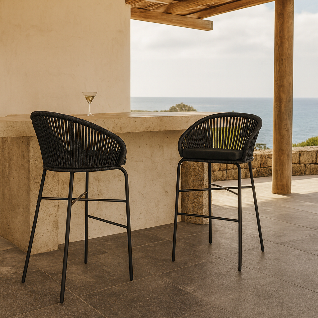 Black rope outdoor bar stools with curved backs styled at a stone bar on a coastal balcony, overlooking the ocean with timber posts and a tiled floor