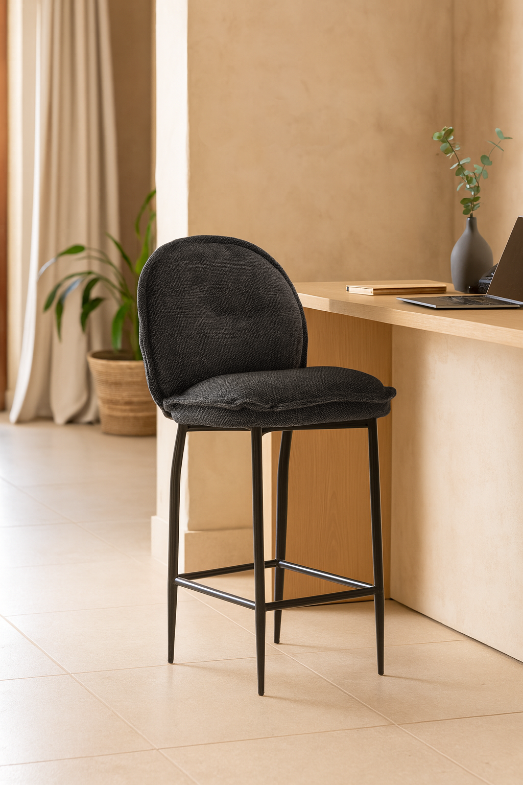Black upholstered barstool with slim metal legs, styled beside a light wood counter in a neutral-toned room with natural light and minimal decor.