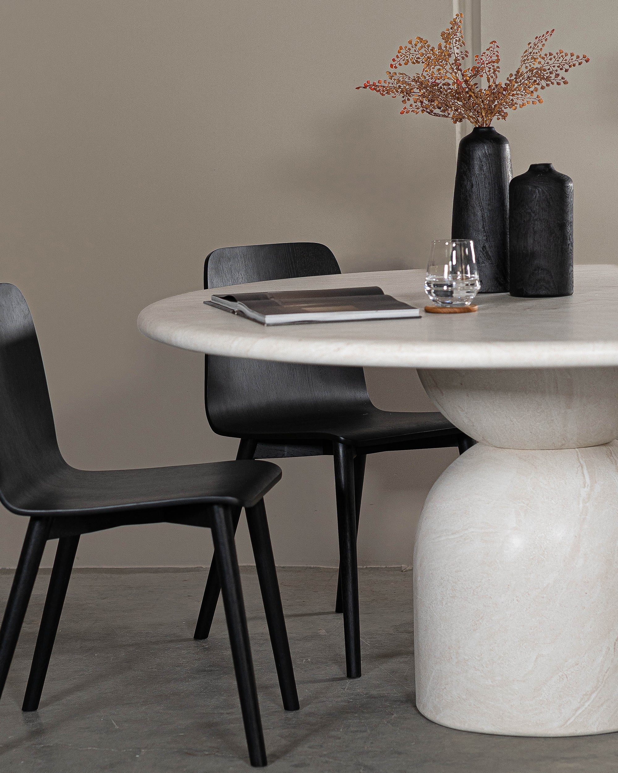 A sophisticated dining setting featuring Kulala Living black wood dining chairs paired with a sculptural marble dining table. The contemporary space is styled with black ceramic vases, dried foliage, and a minimalist aesthetic