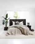 A modern bedroom featuring a black woven bedhead with geometric detailing, complemented by soft linen bedding in natural tones, textured cushions, and a neutral woven rug.