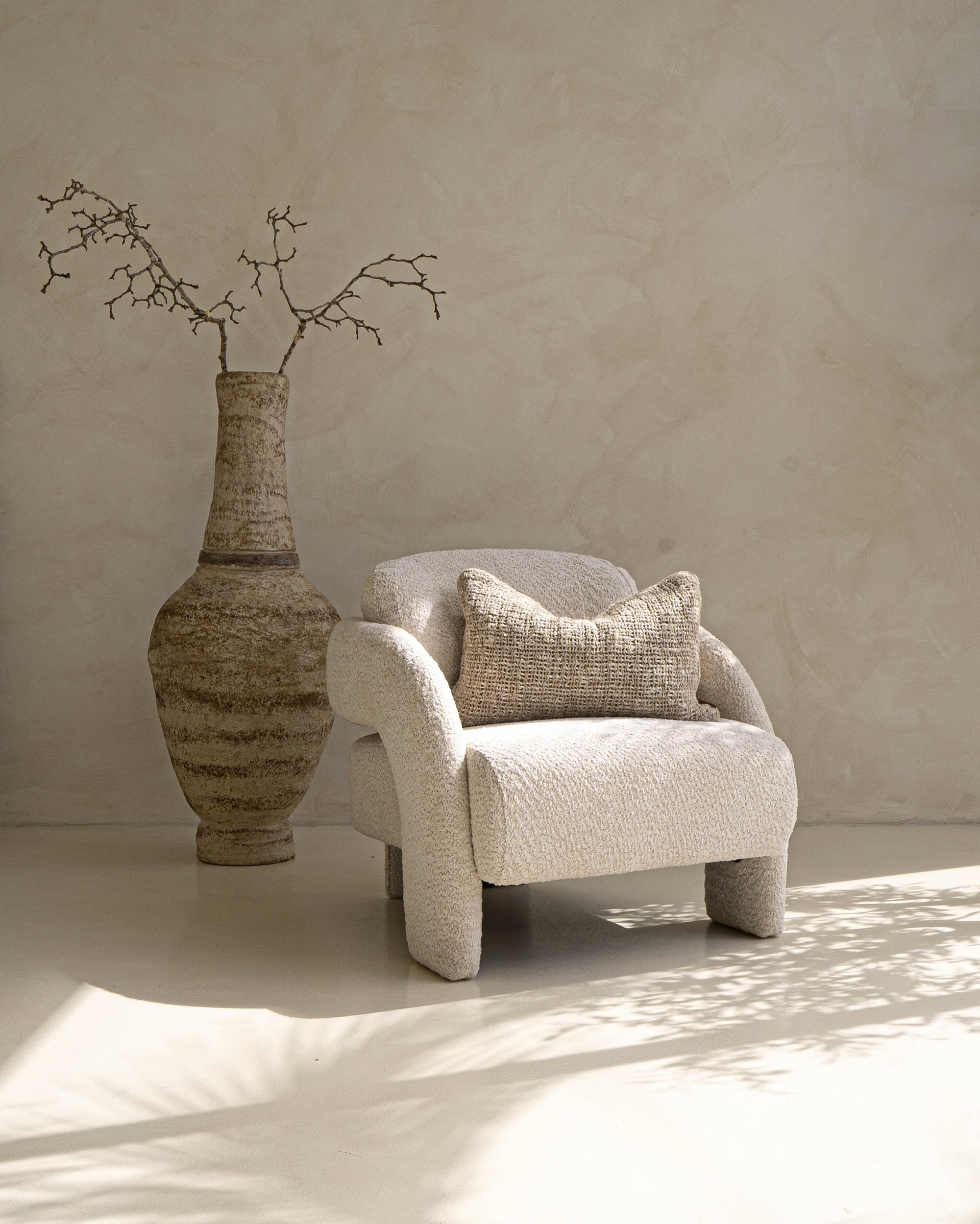 Ivory boucle armchair with rounded, sculptural design, styled with a textured cushion and oversized ceramic vase, creating a serene modern lounge atmosphere.
