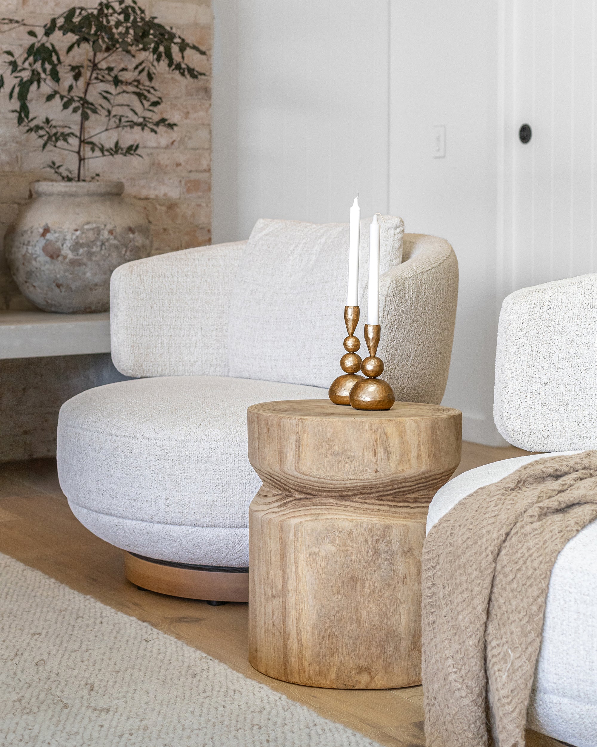 A beautifully styled living space featuring KULALA Living’s brass candlestick holders on a sculptural wooden side table. The warm, neutral tones of the boucle swivel chair, soft throw, and textured rug create an inviting and sophisticated setting with organic elegance