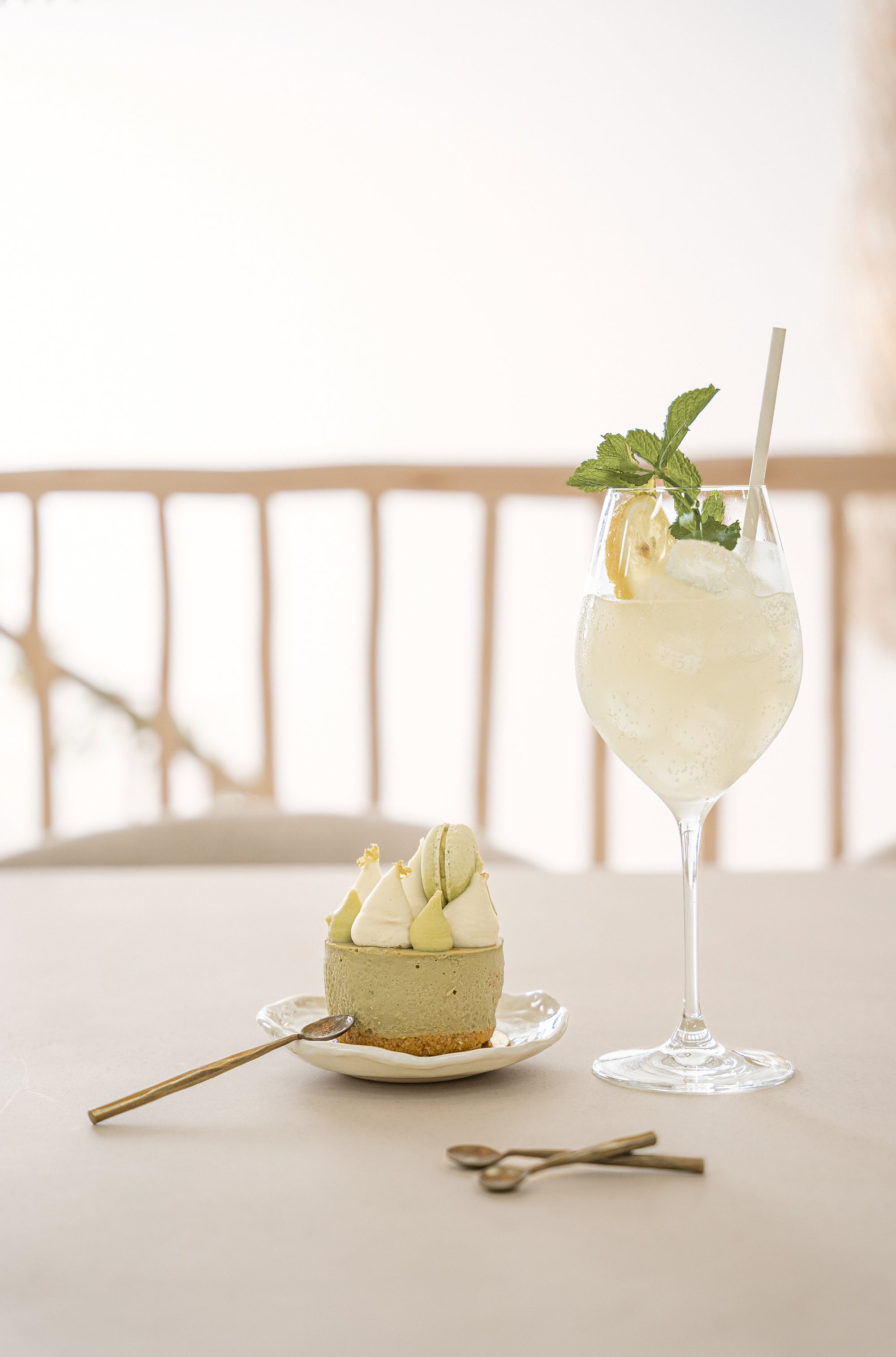 A beautifully styled dessert scene featuring KULALA Living brass dessert spoons, a matcha cheesecake, and a refreshing citrus cocktail. The elegant setting exudes a warm, inviting atmosphere perfect for slow living and indulgence