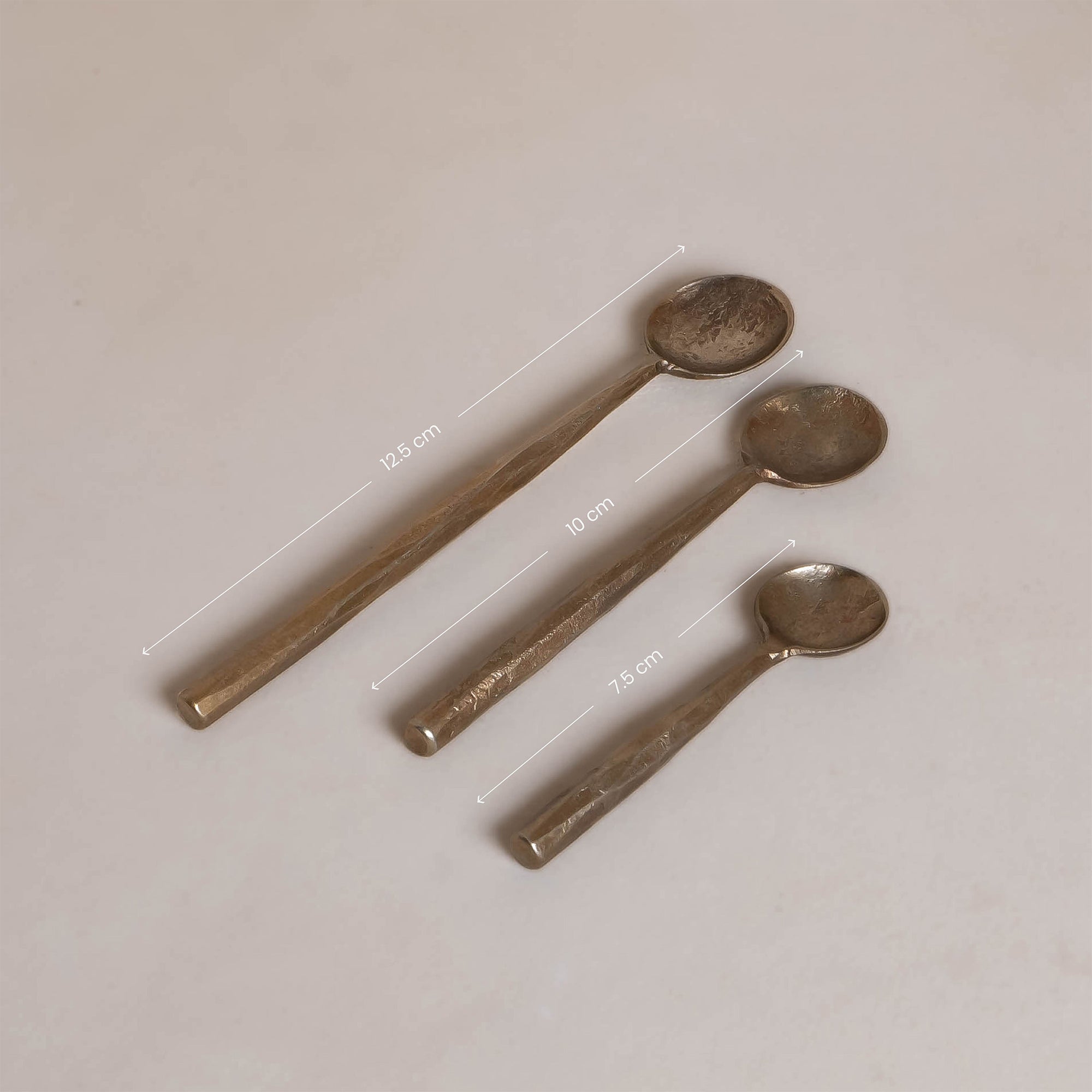 A set of three handcrafted brass spoons from KULALA Living, featuring an artisanal hammered finish and elegantly tapered handles, perfect for serving and stirring with style