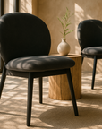 Bronson dining chair in black upholstery styled in a warm modern interior with natural light and timber side table.