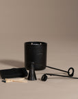 A sophisticated black iron candle care set from KULALA Living, featuring a wick trimmer, candle snuffer, and a box of black-tipped matches, elegantly displayed alongside a black KULALA Living candle