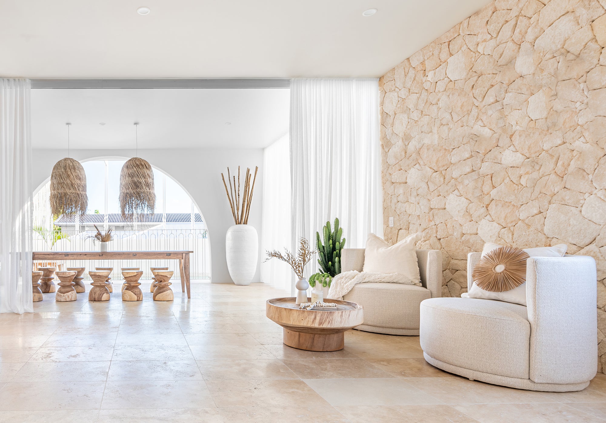 Bright and airy coastal lounge and dining space featuring Kulala Living rattan furniture, neutral-toned boucle armchairs, wooden coffee table, and pendant lighting. A serene and stylish interior design