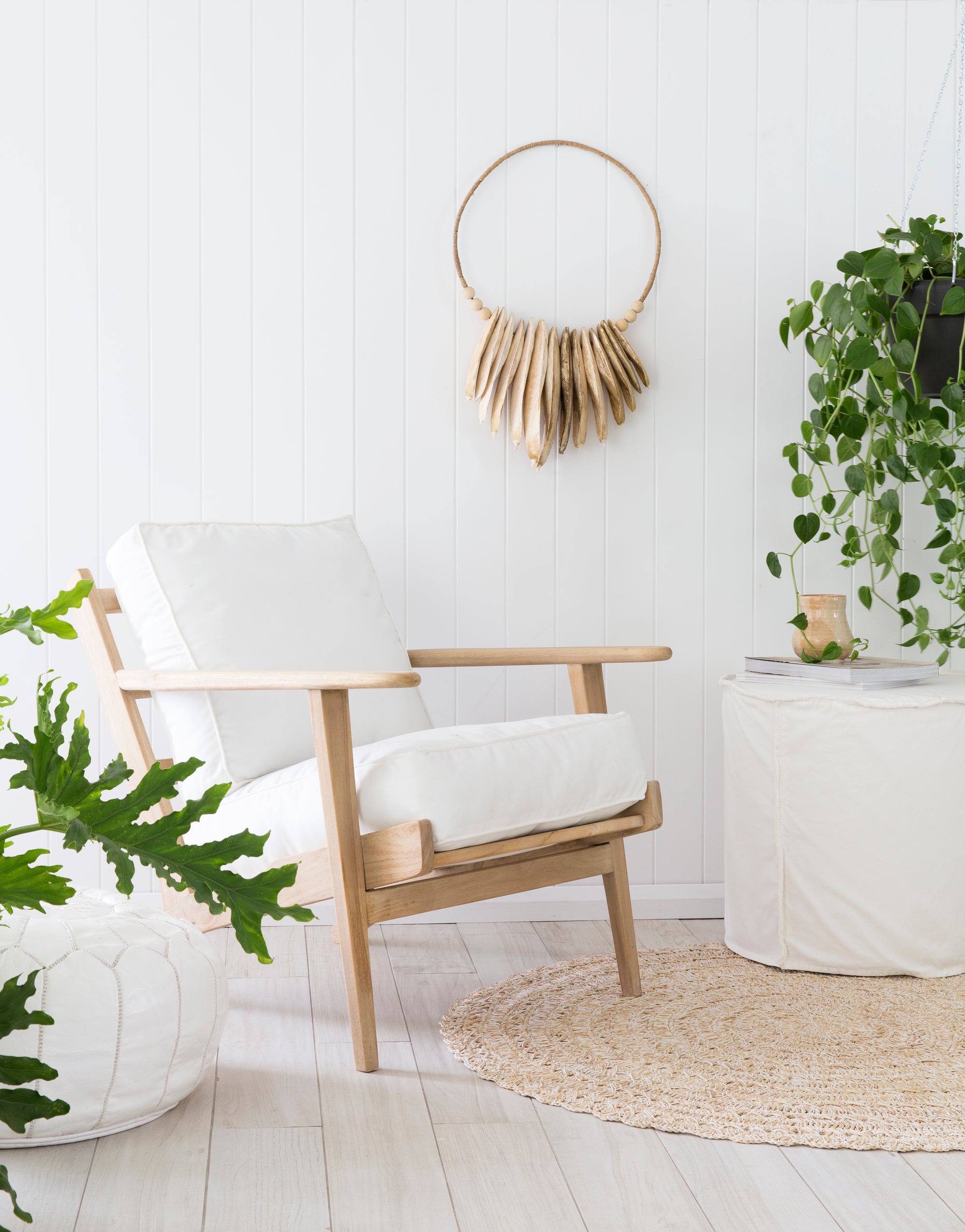 A serene coastal living space featuring a white slipcover sofa, natural woven cushions, and a linen slipcover ottoman. The setting is complemented by a rattan rug, wooden accents, and lush greenery, creating a relaxed and inviting atmosphere.