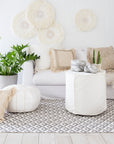 A serene coastal living space featuring a white slipcover sofa, natural woven cushions, and a linen slipcover ottoman. The setting is complemented by a rattan rug, wooden accents, and lush greenery, creating a relaxed and inviting atmosphere.