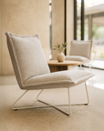Colombia Occasional Chair in natural upholstered fabric with white metal frame styled in a contemporary light-filled living space
