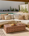 Concrete modern outdoor coffee table with perforated design, styled poolside with a white curved lounge, neutral cushions, and timber pergola