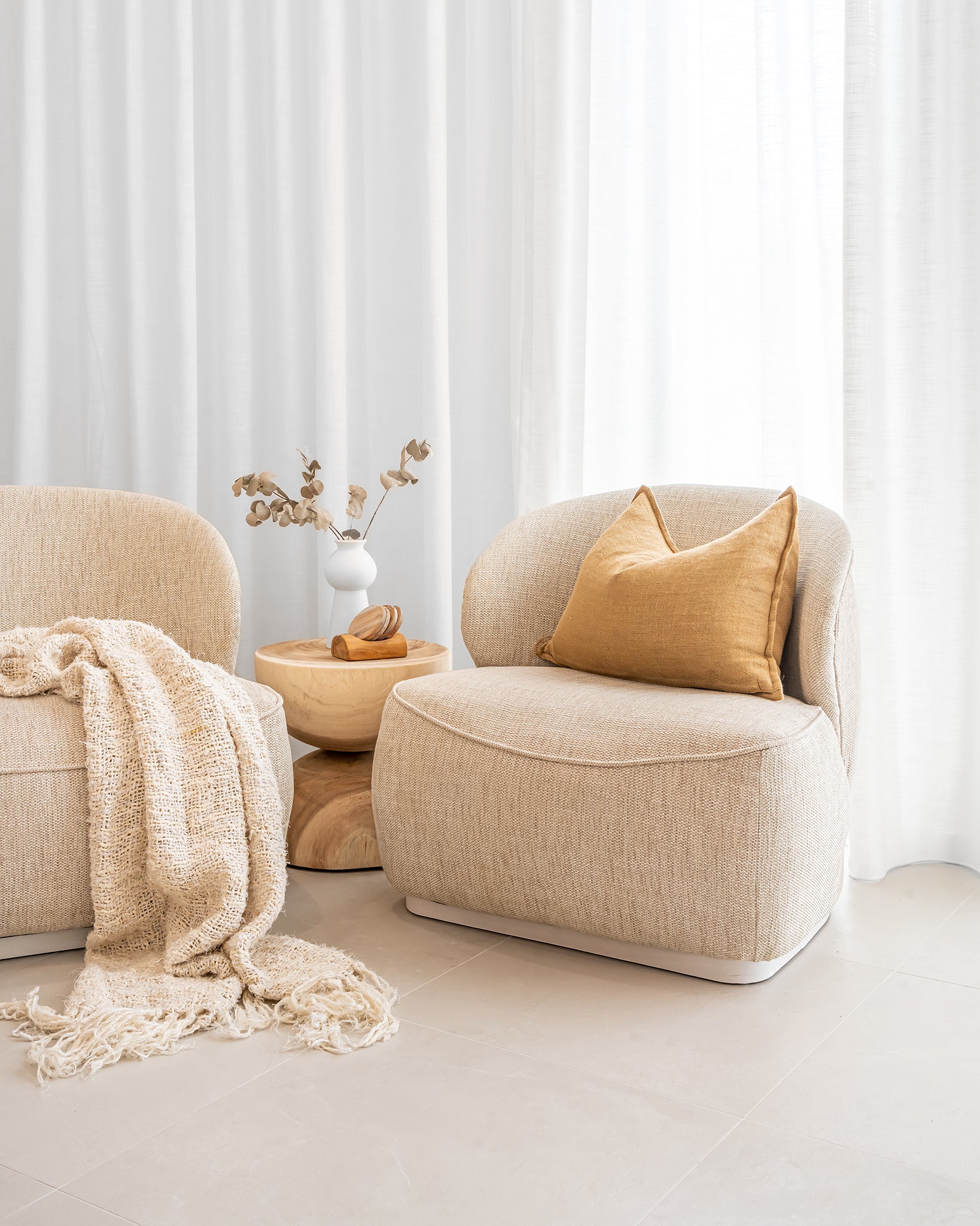 Coroo occasional chair in natural textured fabric with a soft curved backrest and rounded silhouette on a low plinth base.