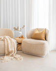Coroo occasional chair in natural textured fabric with a soft curved backrest and rounded silhouette on a low plinth base.