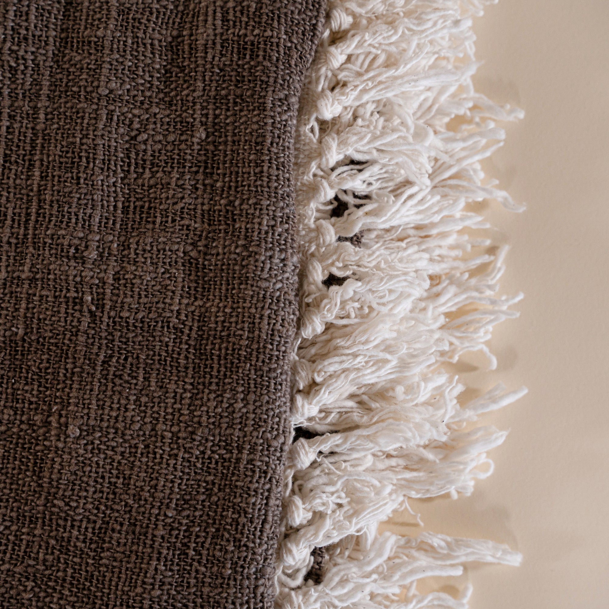 Soft cotton throw blanket in beige and brown with fringe detailing, adding a touch of natural texture to any living space