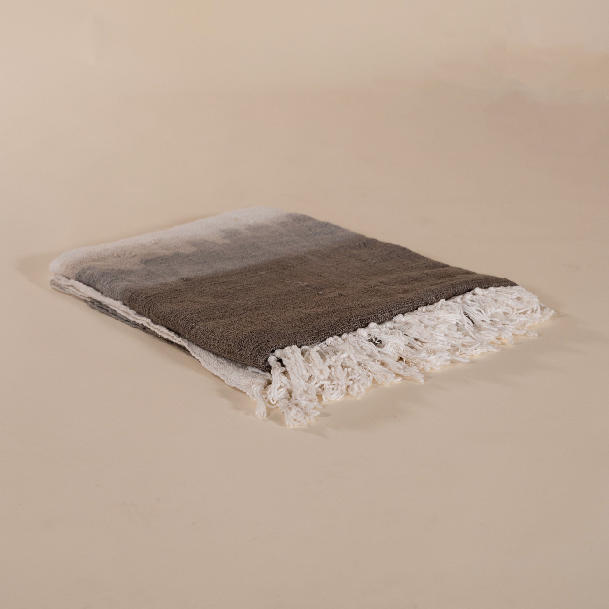 Soft cotton throw blanket in beige and brown with fringe detailing, adding a touch of natural texture to any living space