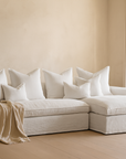 White linen slipcover sofa styled in a neutral living room with layered cushions, soft draped throw and sheer curtains in natural light