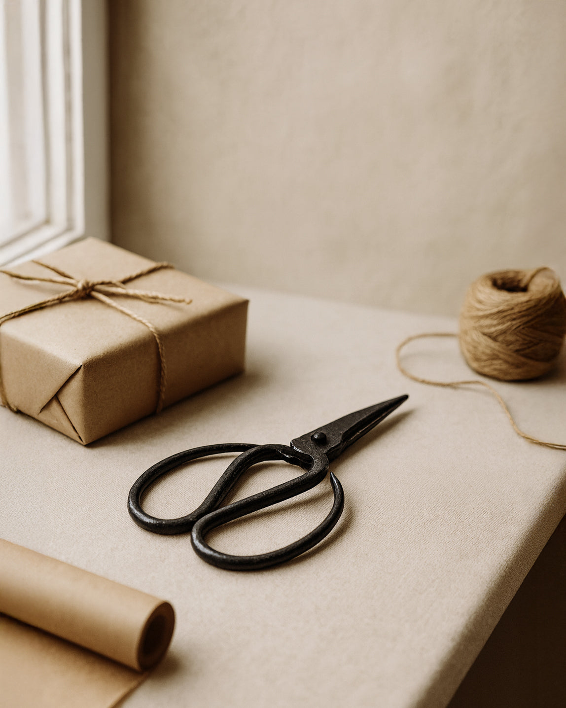 Forged Iron Scissors with handcrafted design styled on a neutral surface beside a wrapped gift, brown paper, and twine in a natural light setting