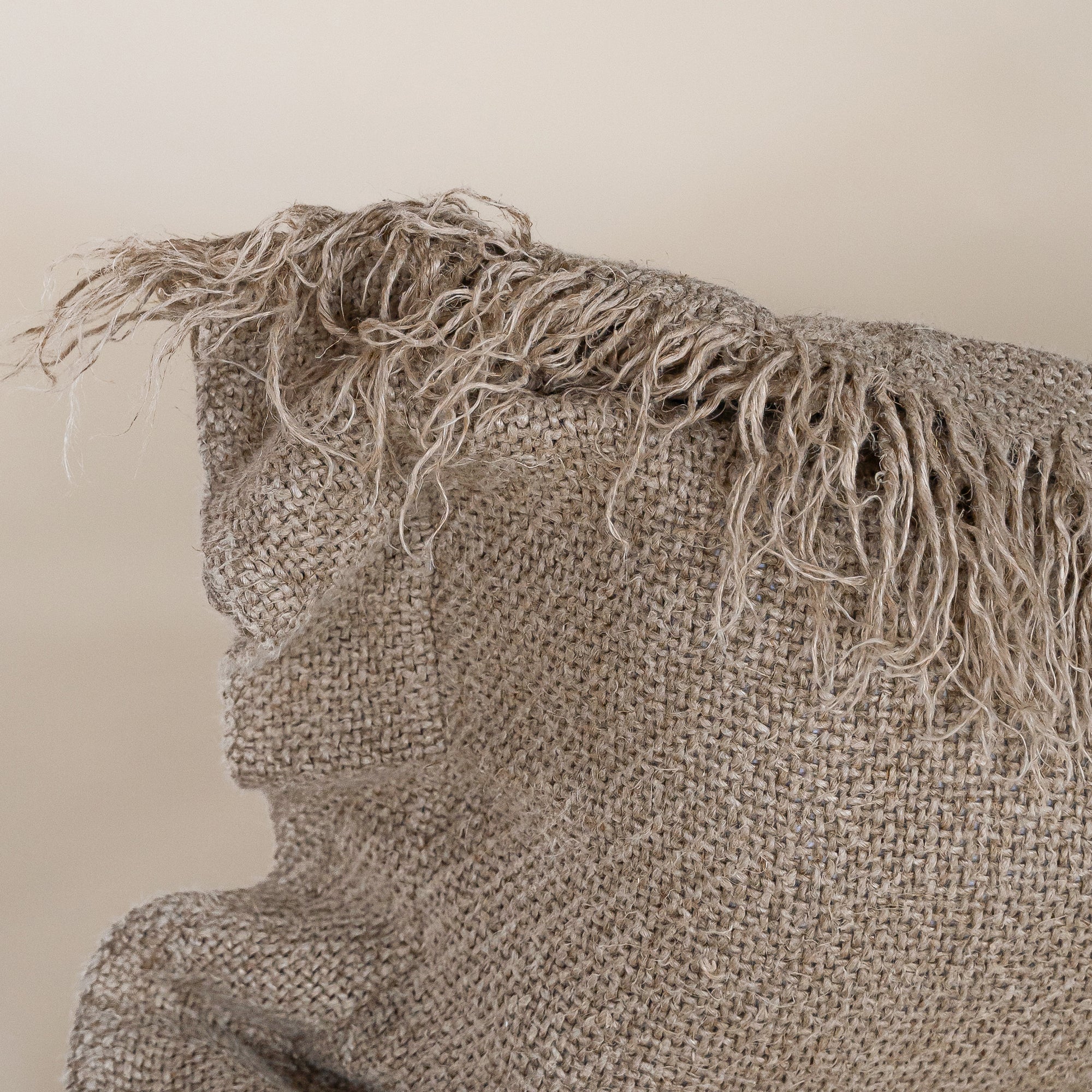 A natural-toned lumbar cushion with a woven texture, featuring delicate fringed edges, set against a neutral backdrop
