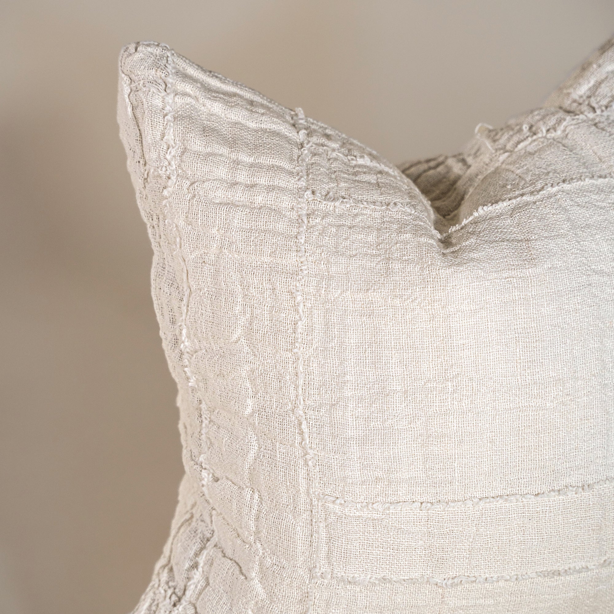 Soft off-white linen cushion with a hand-stitched patchwork design, adding texture and warmth to any living space