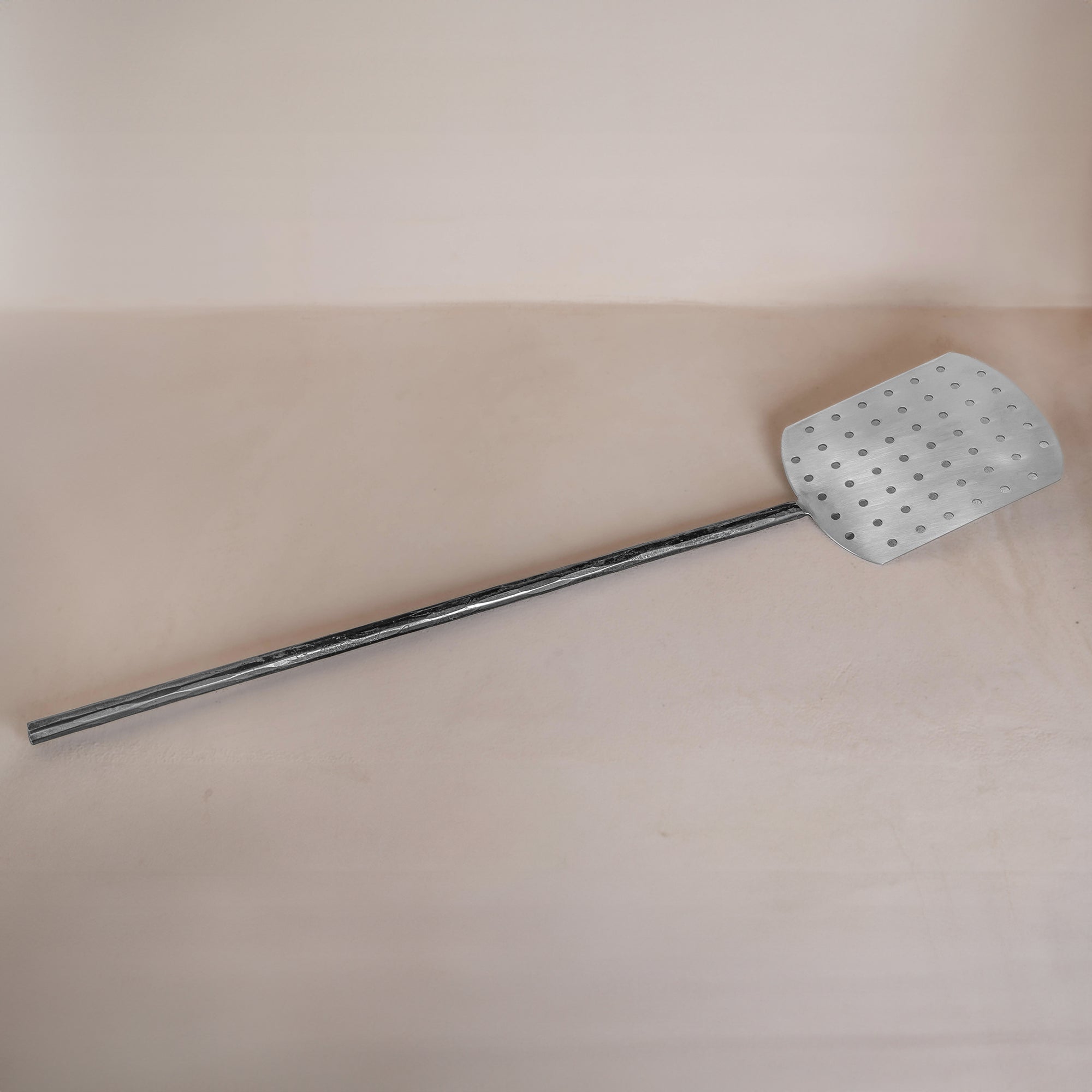 A handcrafted metal spatula from KULALA Living, featuring a perforated stainless steel paddle and a long black iron handle for effortless pizza baking and serving