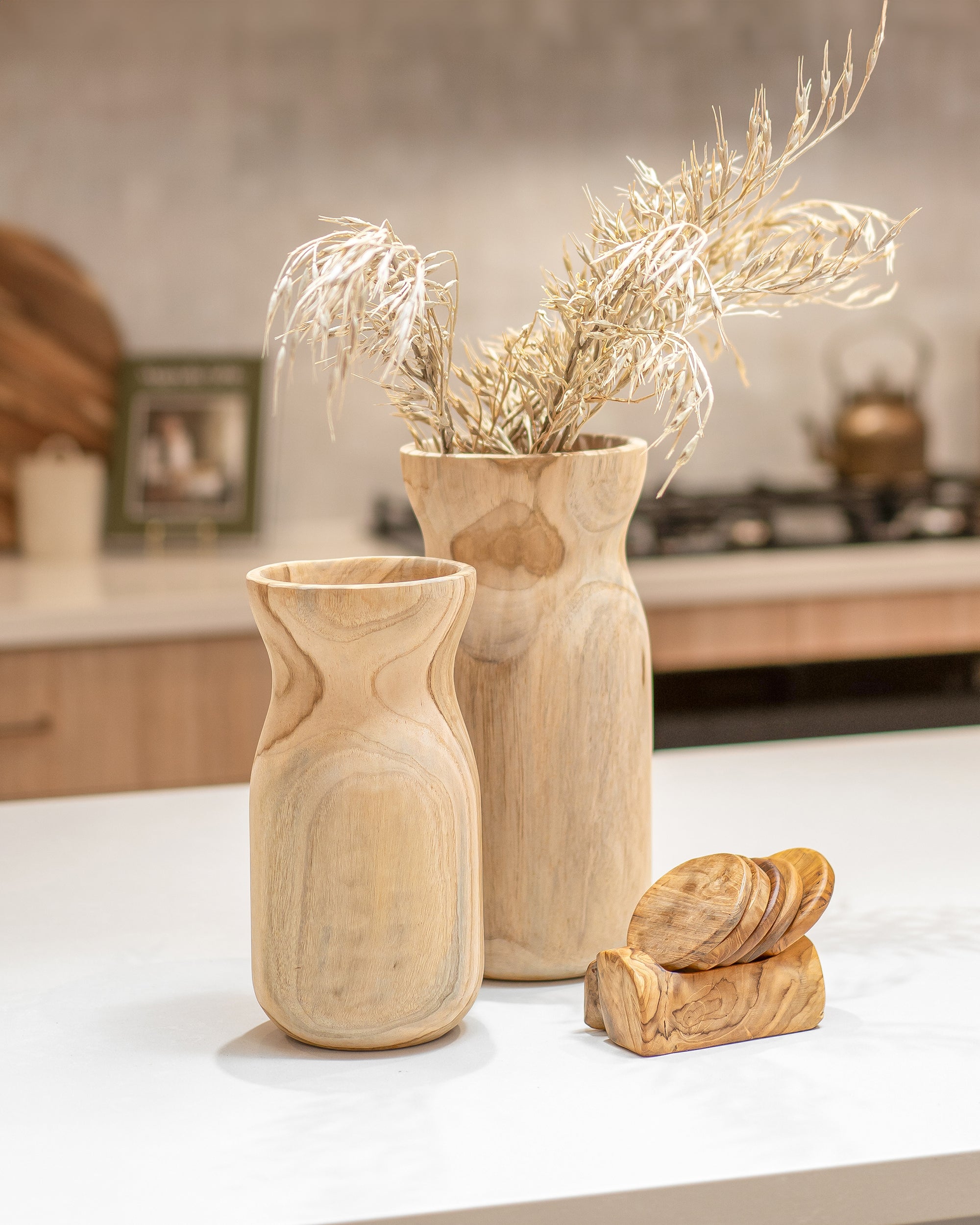 Handcrafted teak vases and coasters styled on a modern kitchen bench, showcasing natural timber grain and organic shapes.