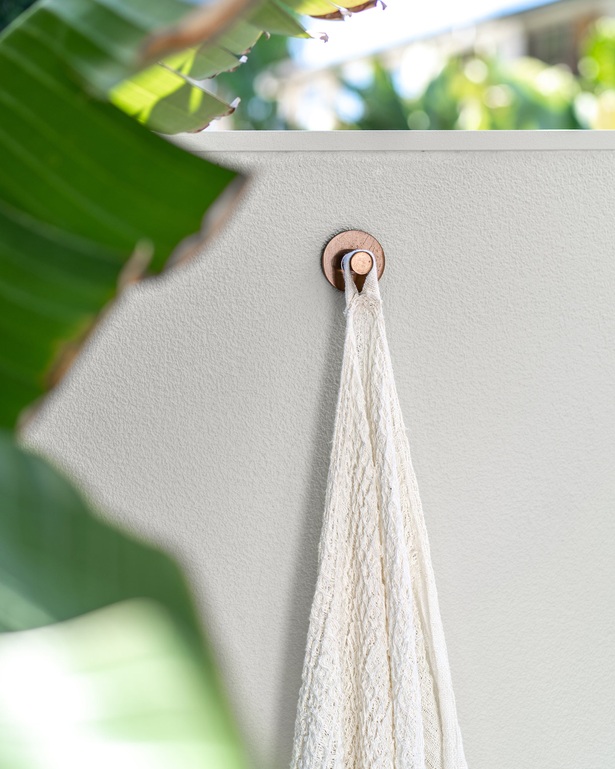 Ivory handloom linen bath towel hanging on an outdoor wall beside tropical foliage and timber decking, capturing a relaxed resort-style atmosphere by the pool.