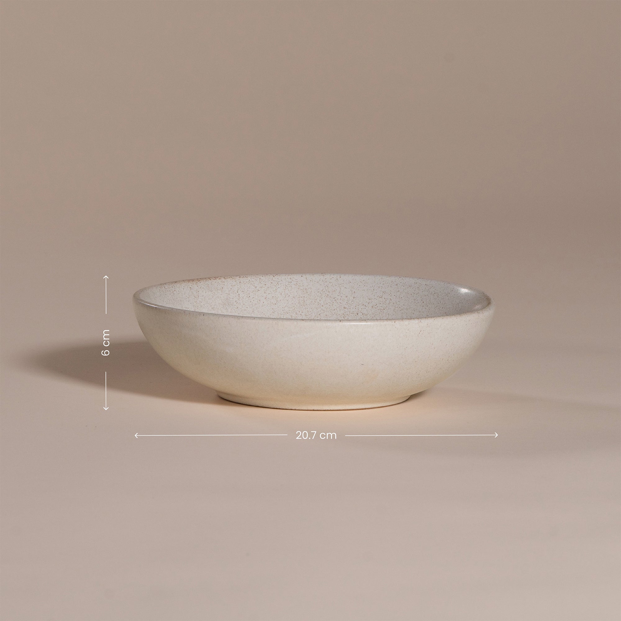 A handmade ceramic bowl with a smooth, speckled neutral glaze, set against a soft beige background. The minimalist design and organic shape make it a versatile piece for modern dining and home decor