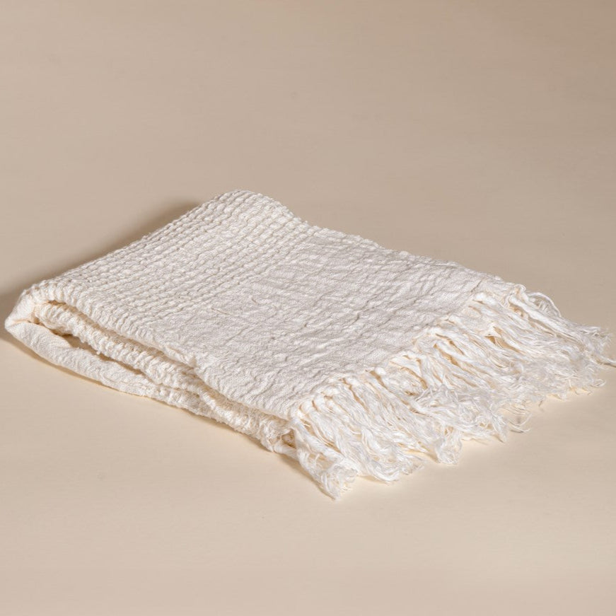An elegant off-white handwoven linen throw from KULALA Living, featuring a soft texture and delicate fringed edges. A perfect layering piece for a relaxed, stylish home