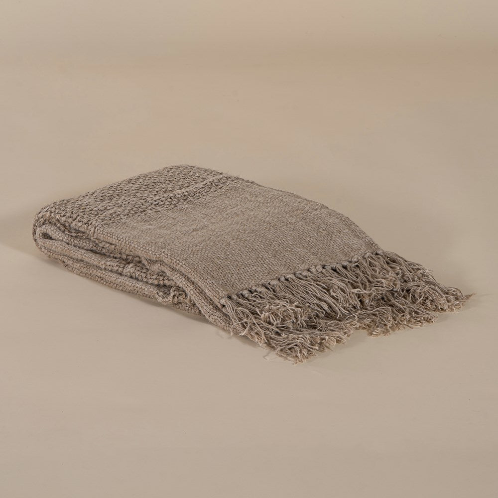 Handwoven natural fibre throw with intricate texture and fringed edges, folded elegantly against a neutral backdrop