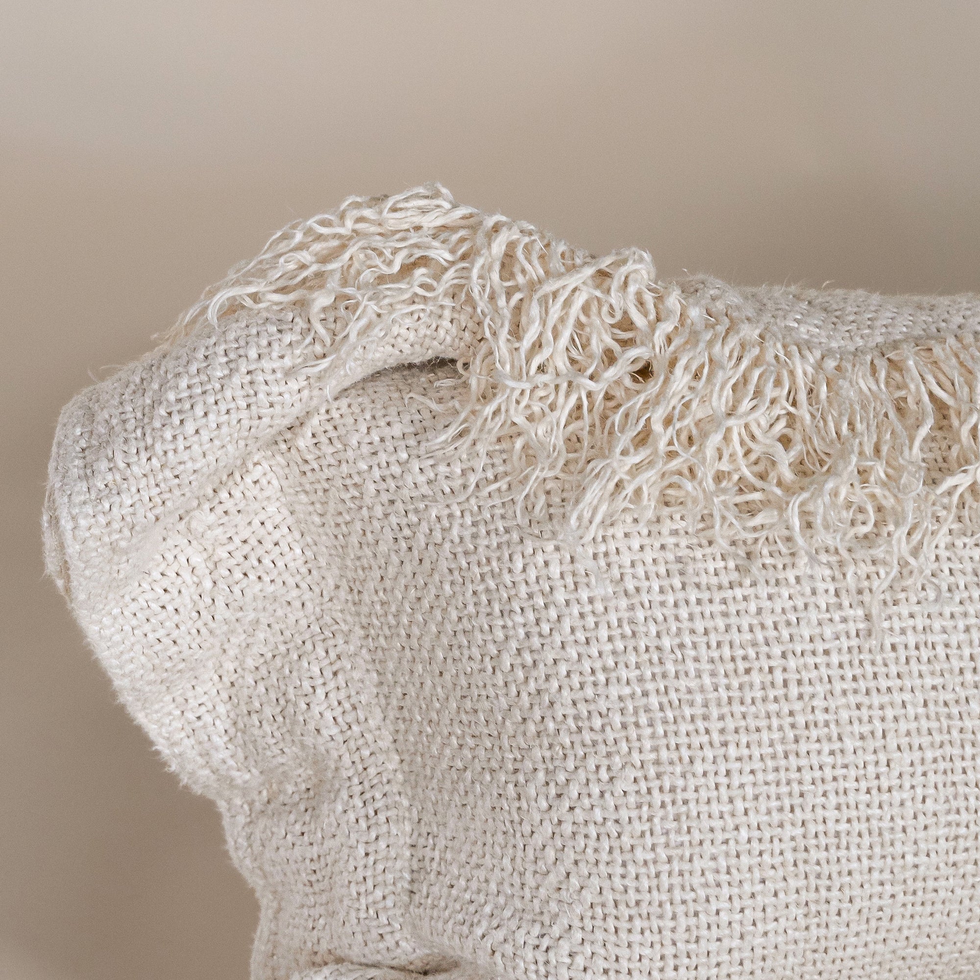 A natural-toned lumbar cushion with a woven texture, featuring delicate fringed edges, set against a neutral backdrop