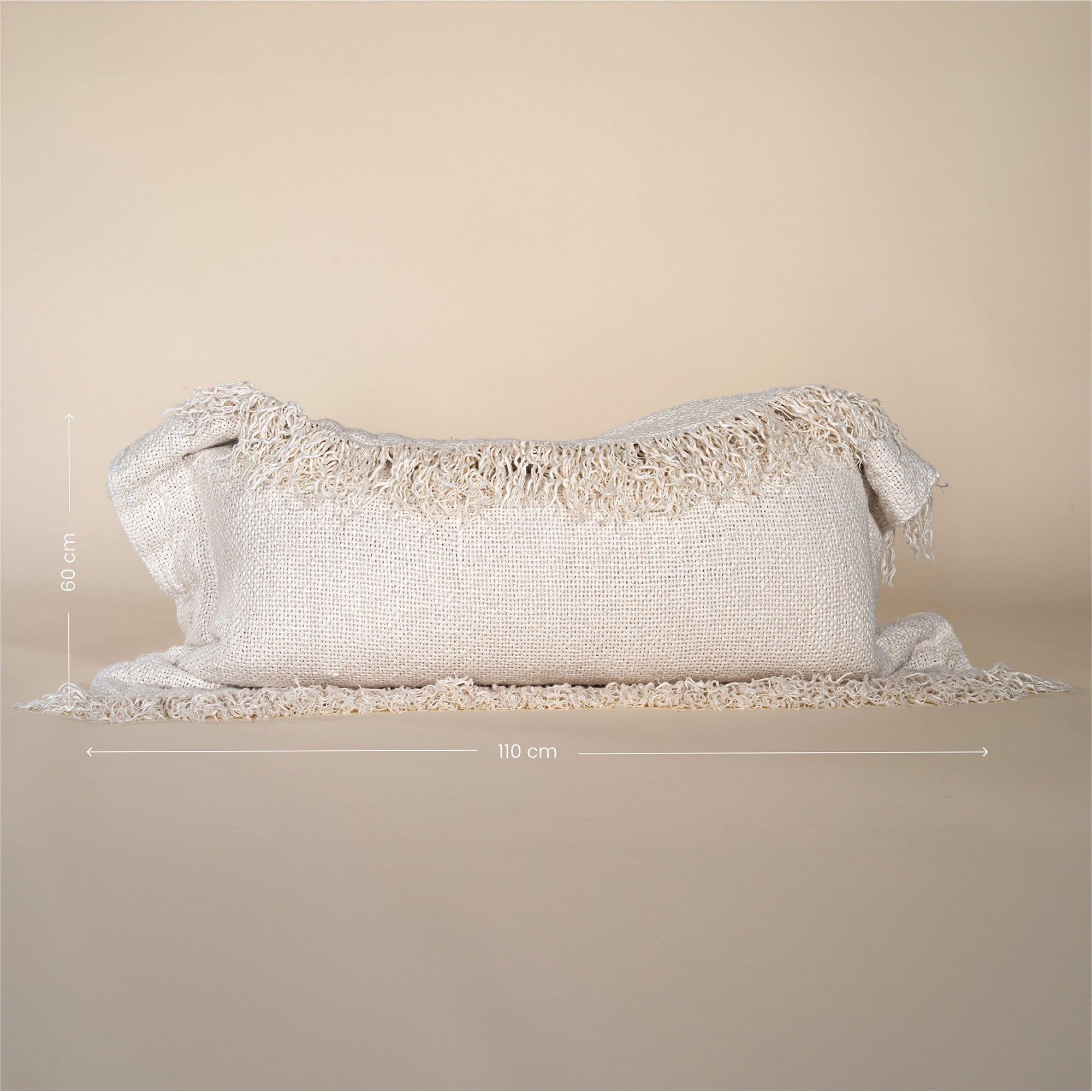 A natural-toned lumbar cushion with a woven texture, featuring delicate fringed edges, set against a neutral backdrop