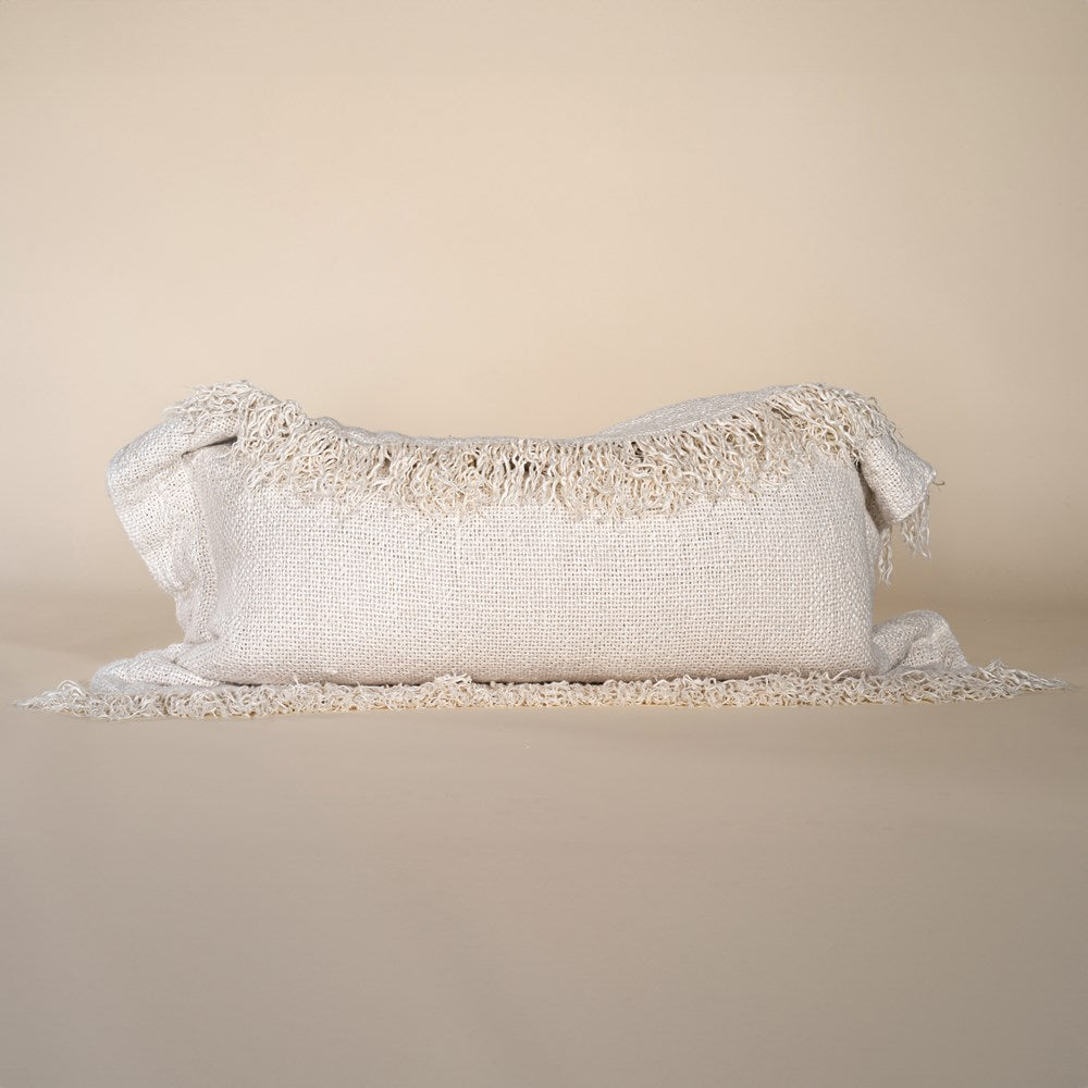 A natural-toned lumbar cushion with a woven texture, featuring delicate fringed edges, set against a neutral backdrop