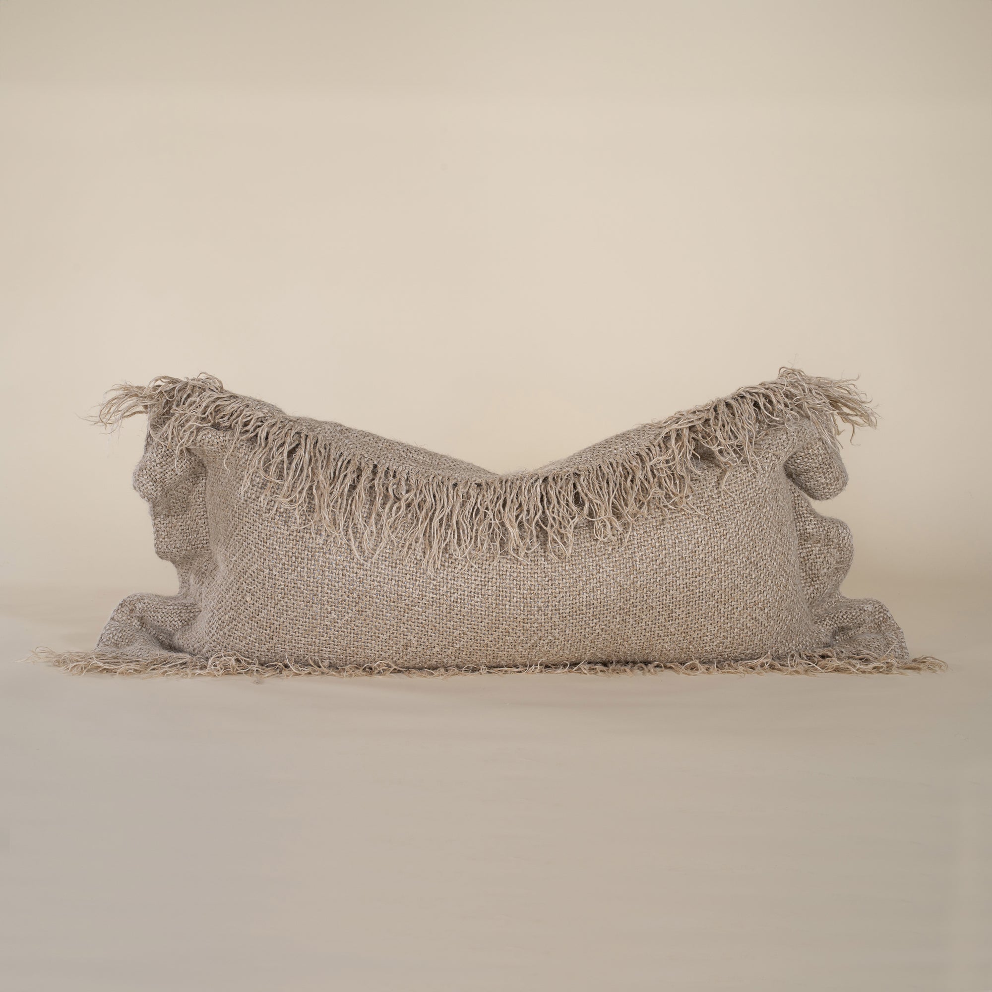 A natural-toned lumbar cushion with a woven texture, featuring delicate fringed edges, set against a neutral backdrop