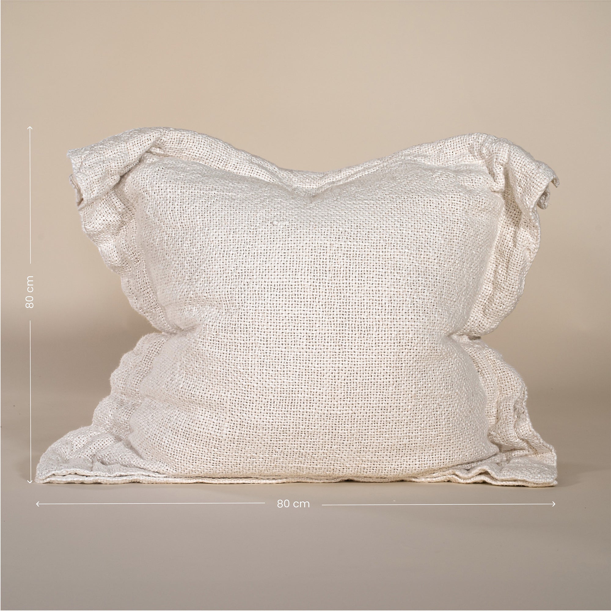 A textured linen cushion in a natural beige tone, featuring a relaxed, oversized design with raw-edge detailing, set against a neutral backdrop
