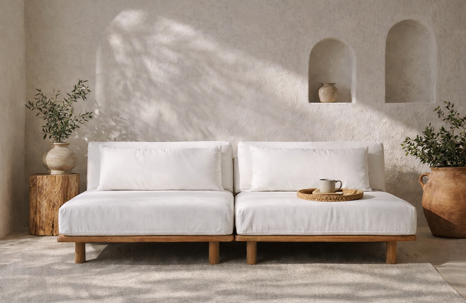 Janelle sofa with low natural timber base and soft white cushions, styled in a warm textured interior with earthy pottery and filtered sunlight.
