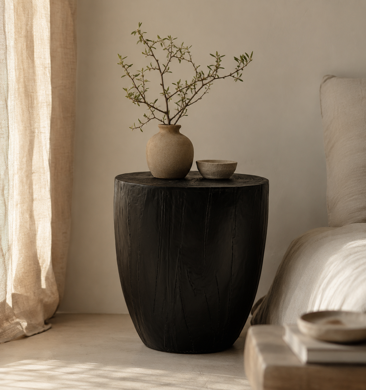 Kisiki Stool in black timber adds sculptural warmth and natural texture beside a relaxed neutral bedroom setting