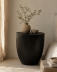 Kisiki Stool in black timber adds sculptural warmth and natural texture beside a relaxed neutral bedroom setting