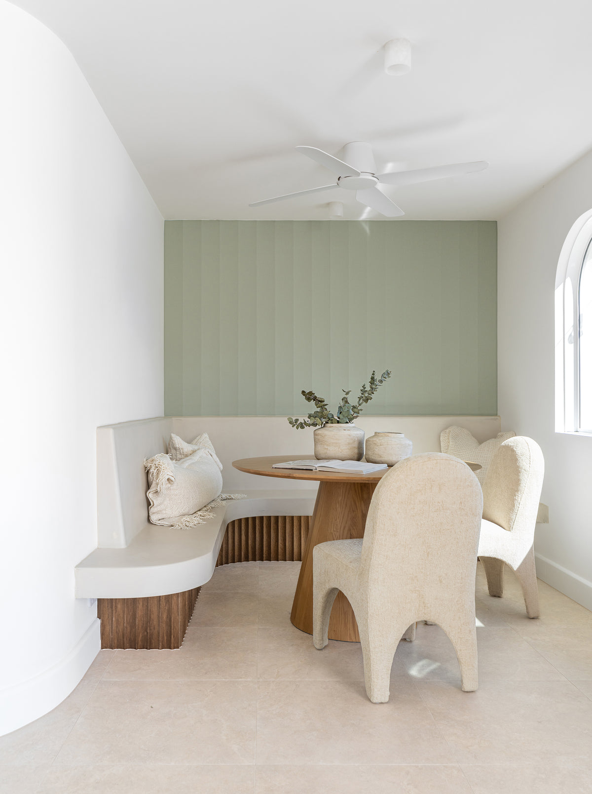 KULALA Living Kuba Oak Dining Table with Tucan Curved Dining Chairs in Chai, Harvest Knotted Cushion and Ibhodwe Terracotta Pots styled in a light filled dining nook with curved built in seating and soft sage green walls.