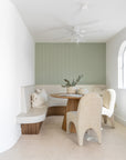 KULALA Living Kuba Oak Dining Table with Tucan Curved Dining Chairs in Chai, Harvest Knotted Cushion and Ibhodwe Terracotta Pots styled in a light filled dining nook with curved built in seating and soft sage green walls.
