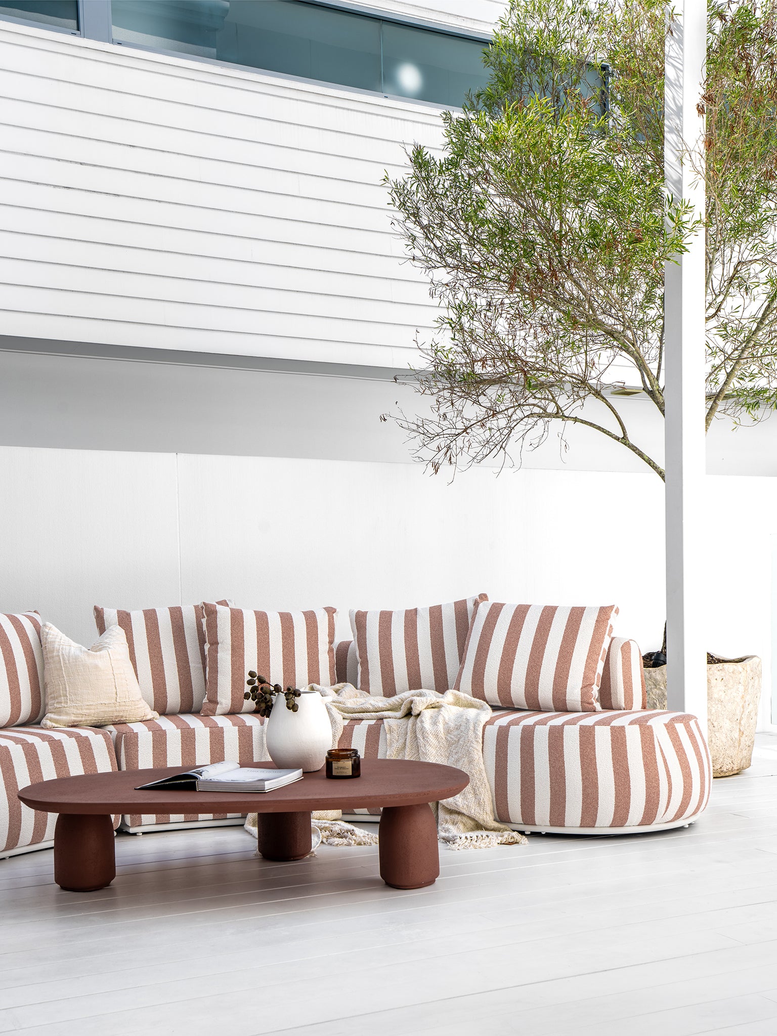 Laguna sofa in cinnabar clay stripe styled with Lantara coffee table and side table creating a warm earthy outdoor living setting.