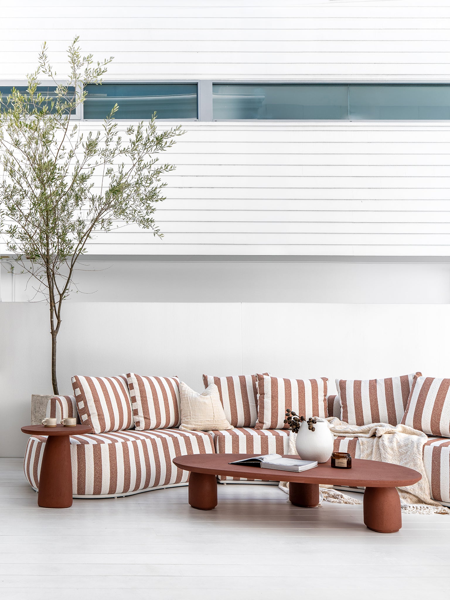 Laguna sofa in cinnabar clay stripe styled with Lantara coffee table and side table creating a warm earthy outdoor living setting.