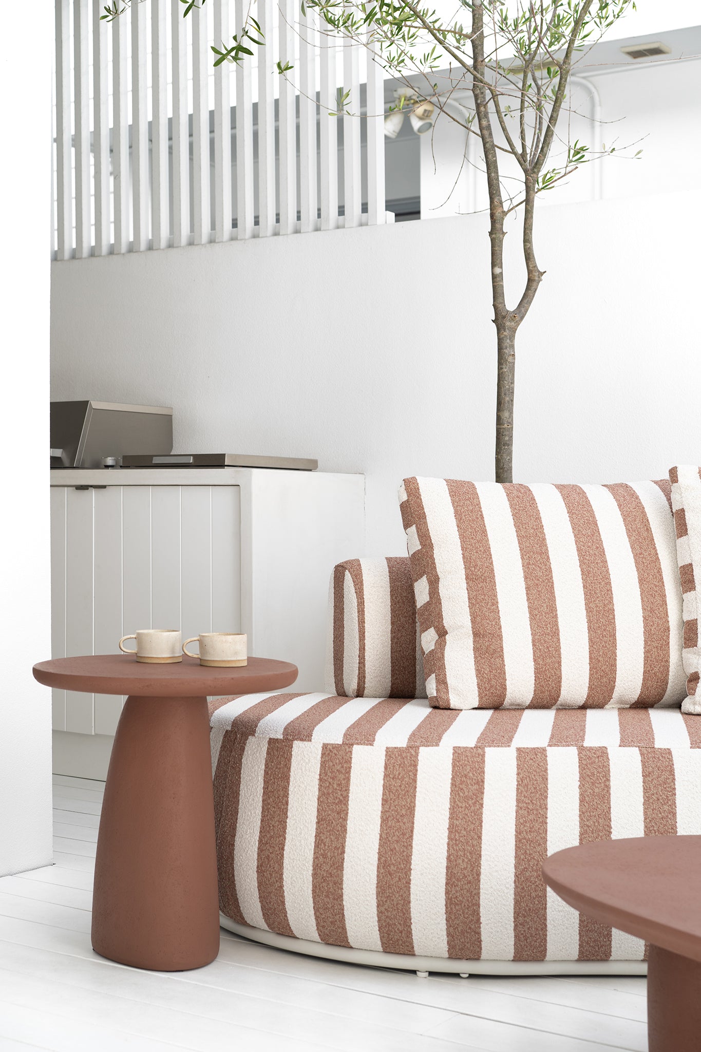 Laguna sofa in cinnabar clay stripe paired with Lantara side table creating a warm relaxed outdoor setting with soft earthy tones.