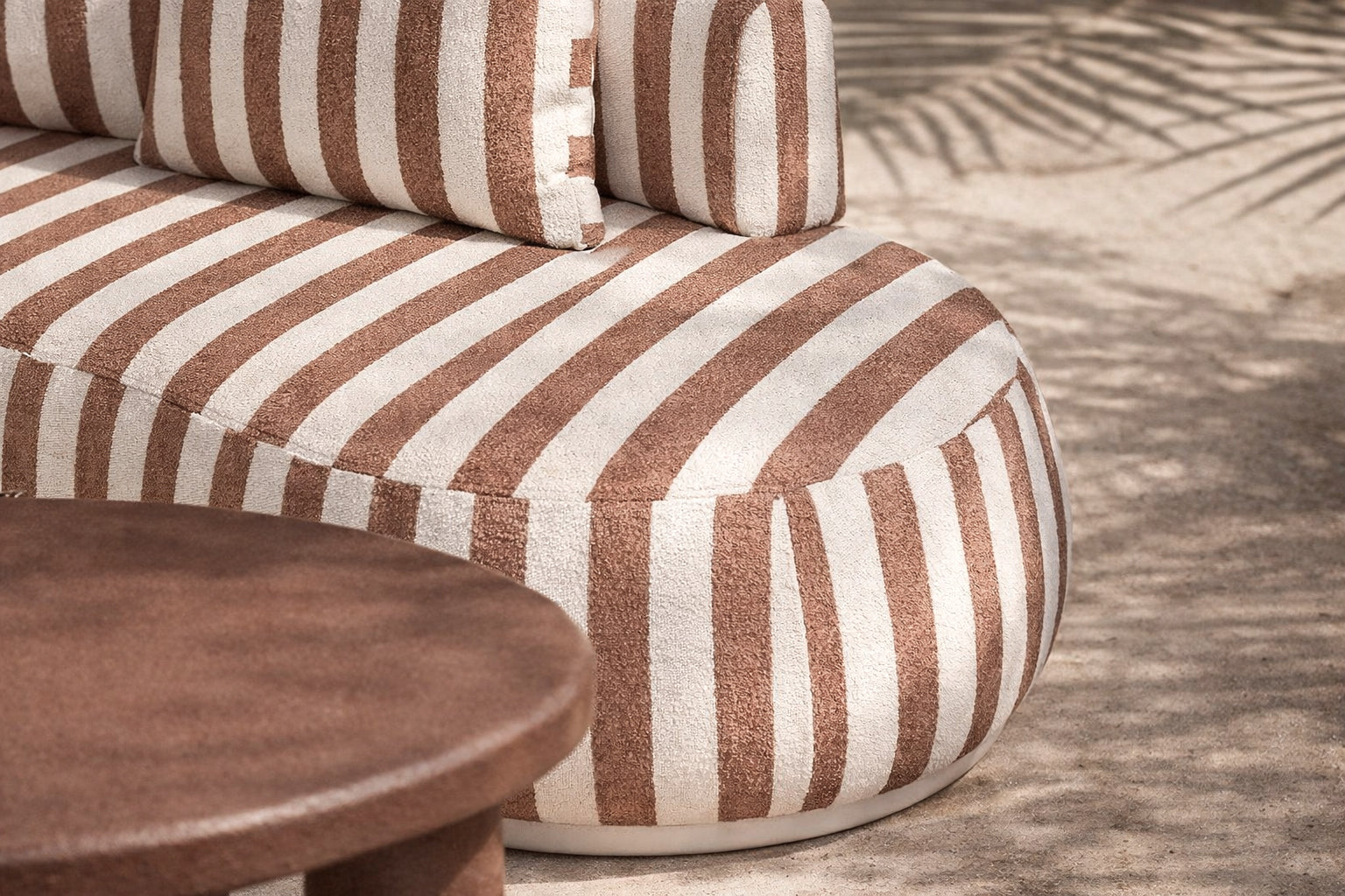 Laguna modular sofa in cinnabar stripe fabric styled outdoors with a lantara coffee table overlooking a coastal view.