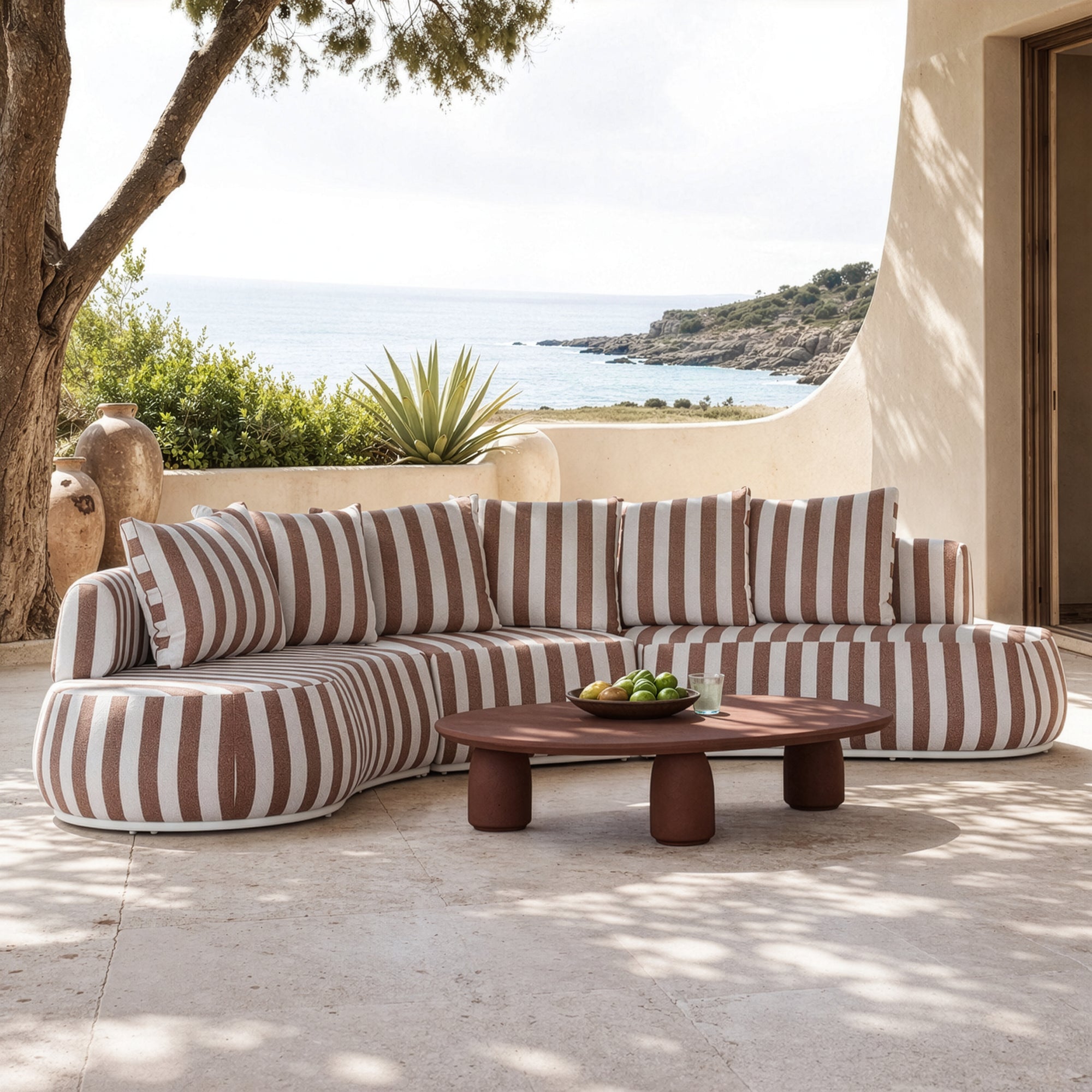 Laguna modular sofa in cinnabar stripe fabric styled outdoors with a lantara coffee table overlooking a coastal view.